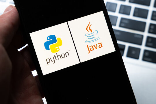 Warsaw, Poland - July 26, 2026: Python and Java programming language logos displayed side by side on smartphone screen held in hand against laptop keyboard background