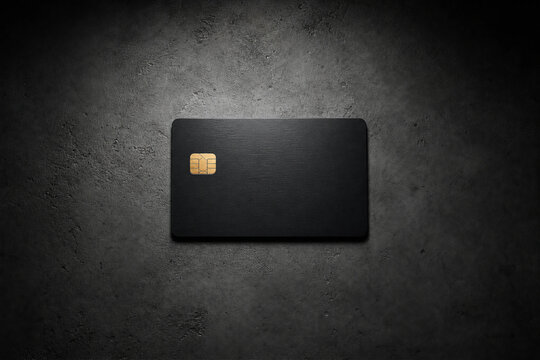 Unbranded matte black credit card with a gold chip on a dark textured concrete background representing luxury banking and financial exclusivity