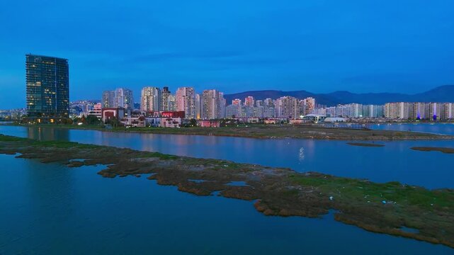 Coastal wetland and salt marsh area near urban waterfront at dusk. Aerial view of natural habitat beside high-rise city development