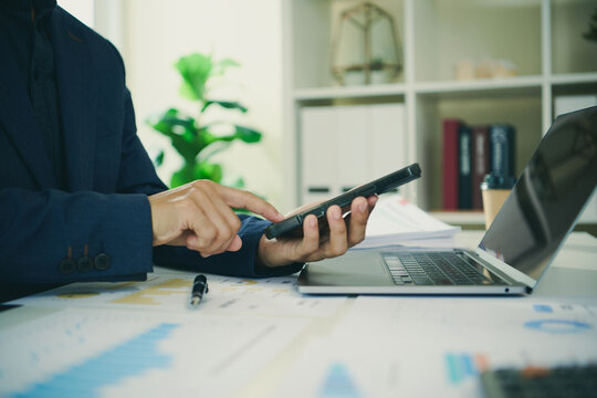 Business financial management with professional using smartphone beside laptop and reports to analyse budgets track performance forecast results and support informed strategic decisions.