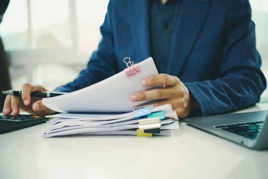 Financial document review with business professional checking organised reports beside laptop to verify records support auditing improve compliance and streamline accurate accounting workflow.