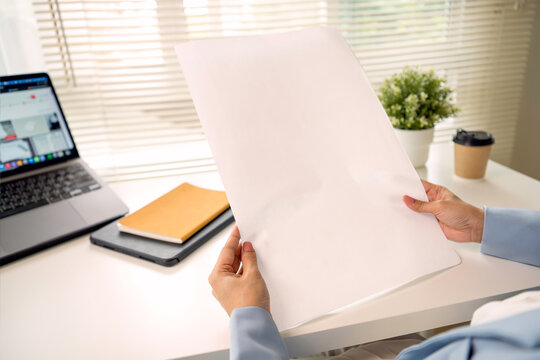 Blank poster mockup held by professional at office desk with laptop providing copy space for advertising presentation branding business communication and creative campaign design.