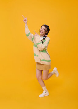 Asian woman pointing upward with joyful expression isolated on yellow studio background promoting positive lifestyle new ideas success celebration advertising and youthful confidence.