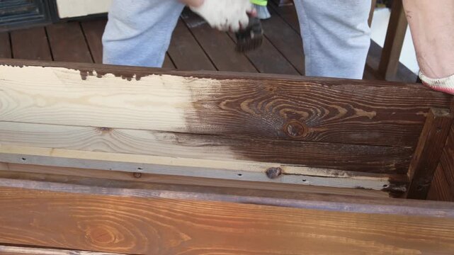 Brown oil for protection of wood by staining. Painting fence for protecting and pests. Woodworker applying finish to pine board box. Repairman varnishing with brush wooden fencing wall plank surface.