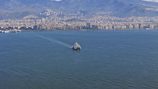 Ferry boat sailing across calm bay near dense coastal city. Urban waterfront, aerial view