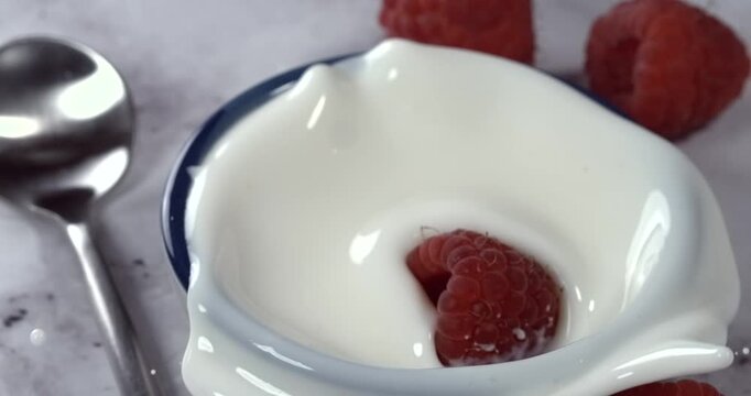 Raspberry falling into a bowl of milk with splash in super slow motion