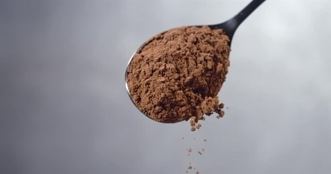 Cocoa powder falling from spoon chocolate dust cloud slow motion