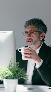 Video of elegant businessman drinking coffee while working on a computer in the office