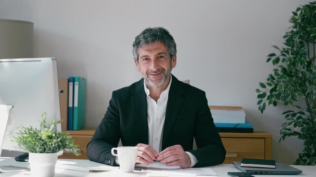 Video of smiling elegant businessman working on a computer while looking at camera in the office
