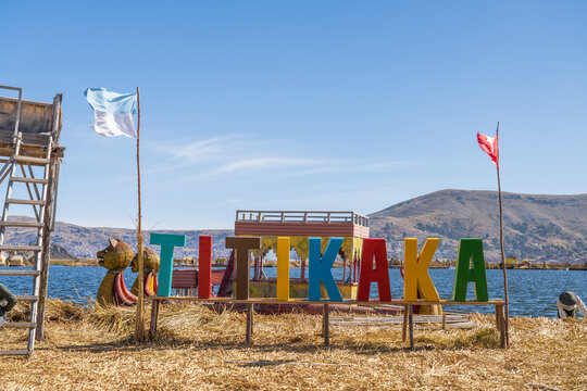 Puno, Peru - June 23rd 2026: Colorful Titikaka tourist sign standing on a traditional Uros floating reed island with a totora reed boat and clear blue skies, Lake Titicaca