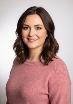 Friendly brunette woman smiling warmly while wearing a soft pink knitted sweater.