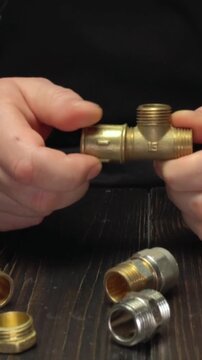 Hands assembling brass plumbing fittings with threaded connections, showcasing a T-joint and various connectors on a wooden surface, emphasizing the detailed craftsmanship and precision in plumbing wo