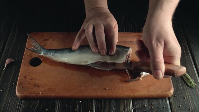Hands of a person skillfully filleting a fish on a wooden cutting board, showcasing the precise cutting technique and the gradual removal of flesh and bones in a well-lit kitchen environment