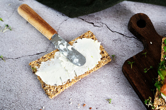 Spreading smooth cream cheese on a multi-grain crispbread with a knife.