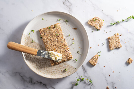Top view of a multi-grain crispbread cracker with cream cheese and knife.