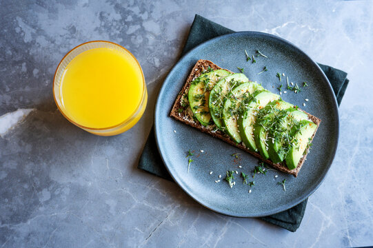 Healthy flat rye bread avocado sandwich and orange juice.