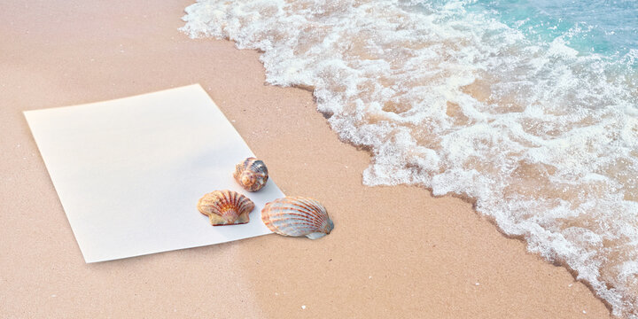 Blank white paper sheet with sea shells on a sandy beach with oncoming sea wave, top view banner