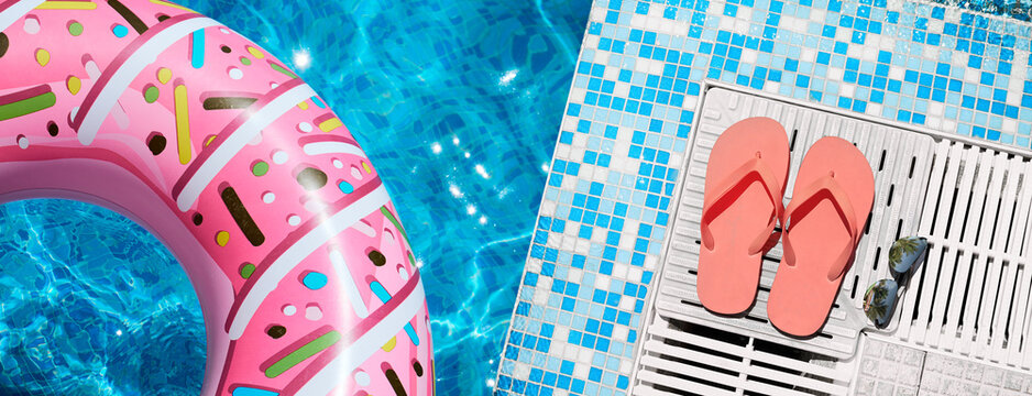 Top view of a colorful inflatable swim ring, flip flops, and sunglasses by a sparkling swimming pool. Bright summer vacation background with copy space for travel and leisure concepts