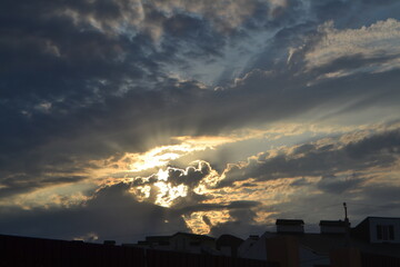 Fototapeta premium Serene sunset over clouds with rays of light and buildings below, concept of atmosphere, sky 