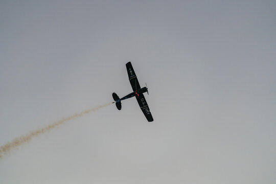 Black stunt airplane performing aerial maneuver with smoke trail