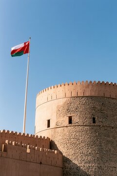 Oman flag waving above a historic fortress against a clear blue sky