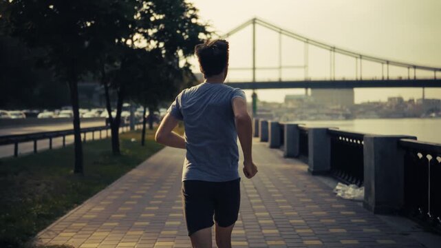 Runner Jogging Along River. Embankment And City Bridge. Workout Outdoor Training 