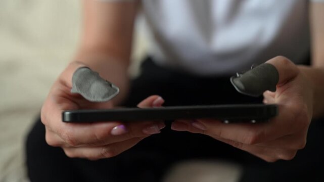 Cropped shot of young woman with fingertips for gaming playing video game on modern mobile phone. Professional cybersport gamer training online with special accessory for better control and precision.