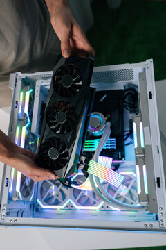 Top view of person upgrading gaming computer, installing powerful graphics card into open pc case, showing internal components with rgb led lighting and custom liquid cooling system, close-up.