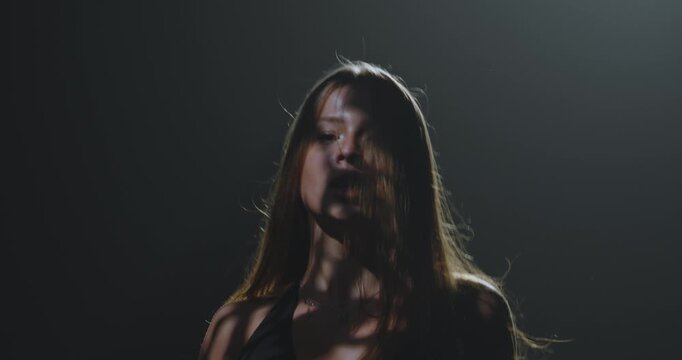 Silhouette of a female dancer performing under a single dramatic overhead spotlight on a dark stage. Concept of dance, performance, nightlife and art, fitness, fashion and entertainment advertising.