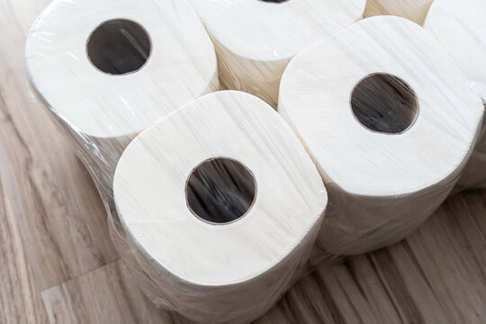 Toilet paper rolls packed in clear plastic wrap stacked on wooden floor, household essential supply concept for home storage and hygiene products