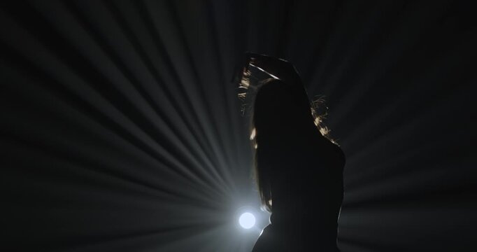 Silhouette of a female dancer performing on a dark stage, back lit by dramatic volumetric light rays with copy space. Concepts related to dance, self discovery, album covers, singles, or podcasts