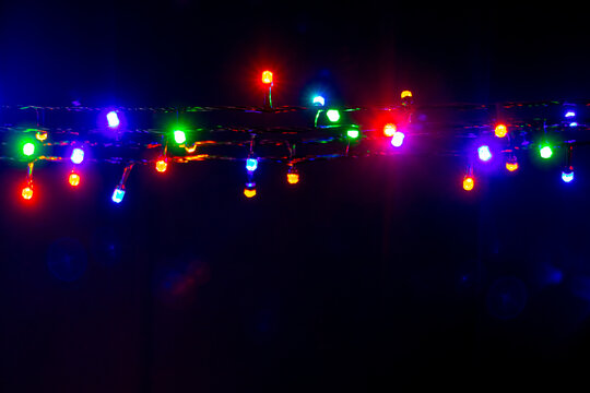 Christmas and New Year garland with bright multi-colored lights on black isolated background, copy space