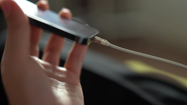 Close-up of female hands plugging white lightning cable into smartphone to charge battery, unplugging, showing connecting and disconnecting device for power and data transfer. Shooting in slow motion.