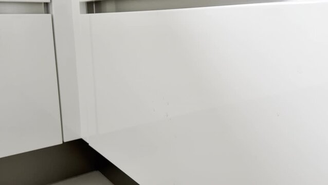 Close-up of a female hand inspecting white kitchen cabinet surface for scratches and imperfections