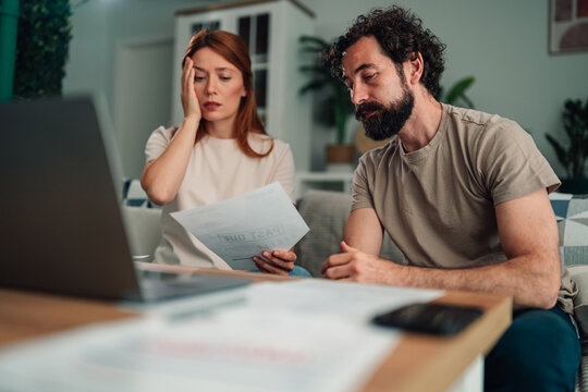 Couple analyzing past due bills and financial paperwork on a laptop at home, experiencing money problems and stress
