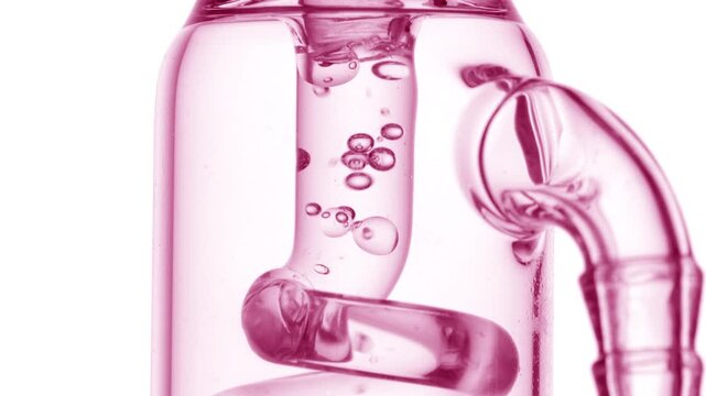 Extreme close-up capture of colorless clear liquid flowing through a glass tube, causing bubbles to condense and chaotically move inside it on clean white surface
