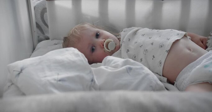 Toddler waking up in nursery bed with pacifier. Child sleep schedule and home bedtime routine