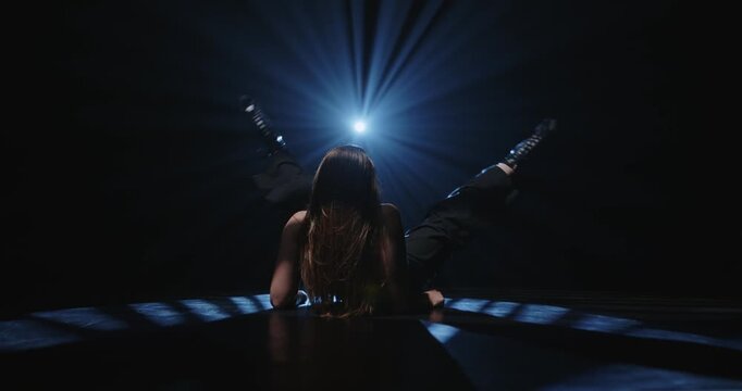 Attractive female dancer posing on floor under bright blue spotlight. Concept of expressive artistic layout for music album cover, theater poster and modern dancing class promotion.