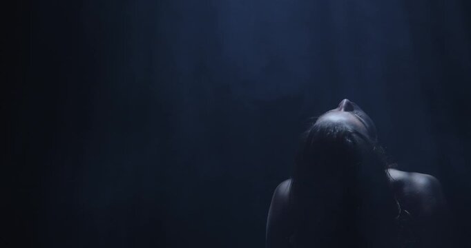 Silhouette of a female dancer performing under a single dramatic overhead spotlight on a dark stage. Concept of dance, performance, nightlife and art, fitness, fashion and entertainment advertising.