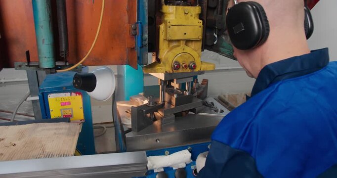 Machine operator working with punch press for metal part production. Industrial stamping equipment in factory