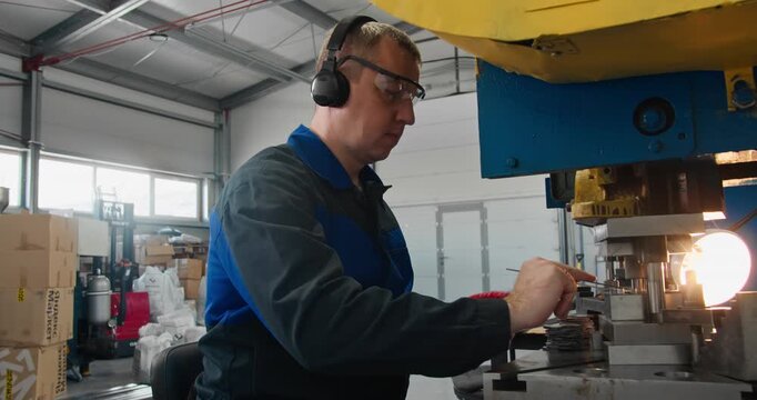 Punch press blue collar worker sorting stamped metal parts. Factory trade occupation with protective eyewear and hearing protection