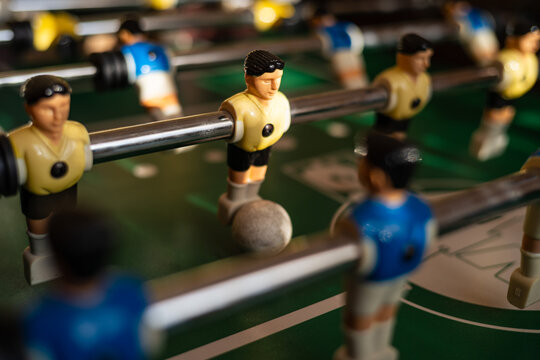 Foosball players competing around the ball on a table football game, representing teamwork, strategy, recreation and competitive indoor entertainment.