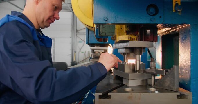 Industrial manufacturing worker operating a punch press and handling finished metal components. Skilled labor concept in close-up