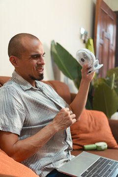Man feeling hot using portable cooling fan at home