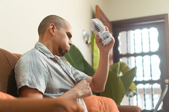 Man feeling hot using portable fan at home