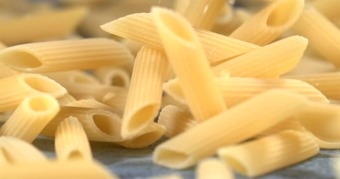 Penne pasta falls bounces and rolls across a blue surface in slow motion