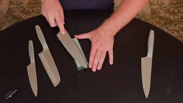 Man sharpening kitchen knife with a stone on a dark table, close-up view