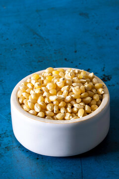 Closeup of un-popped kernels of popcorn with a white ceramic bowl 
