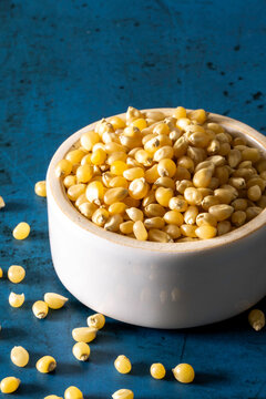 Closeup of un-popped kernels of popcorn with a white ceramic bowl 