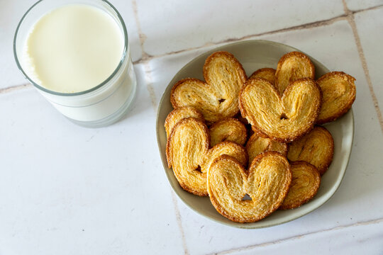 White ceramic plate of Palmiers cookies on a tile countertop and a glass of milk 